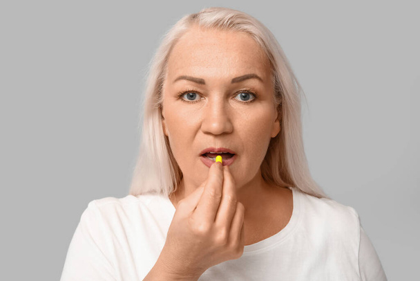 Beautiful mature woman taking pill on grey background - Photo, Image