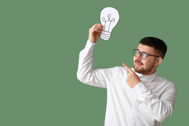 Young businessman pointing at drawn light bulb on green background. Business idea concept - Photo, Image