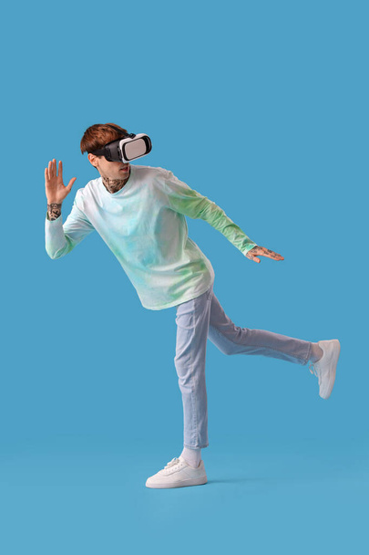Young man in VR glasses running on blue background - Photo, image