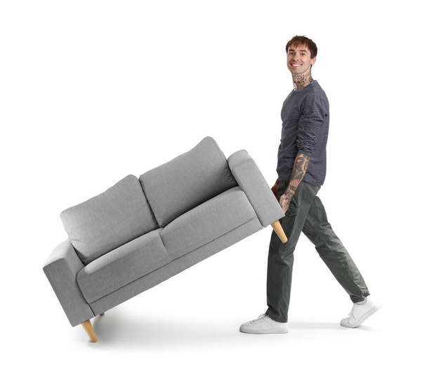 Junger Mann trägt Sofa auf weißem Hintergrund - Foto, Bild