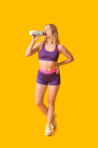 Beautiful sporty woman drinking water on yellow background. Weight loss concept - Photo, Image