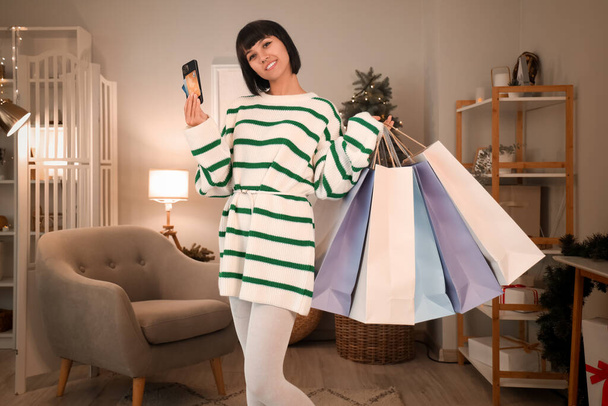 Mladá žena s nákupními taškami, kreditními kartami a mobilním telefonem doma na Štědrý večer - Fotografie, Obrázek