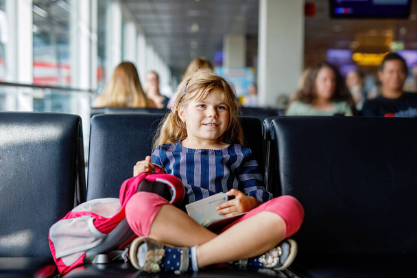 Küçük kız havaalanında büyük pencerede biniş için bekliyor. Pasaportu olan sevimli bir çocuk yaz tatiline gitmeyi dört gözle bekliyor.. - Fotoğraf, Görsel