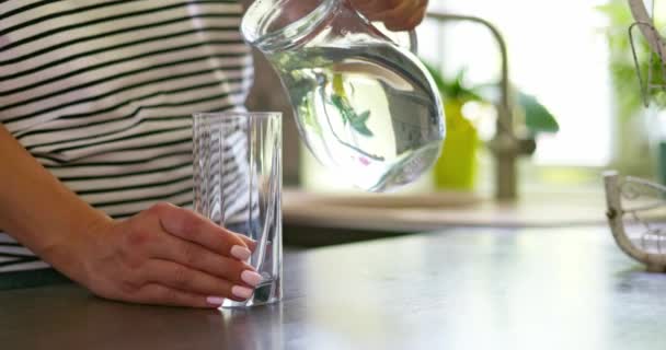 Gros plan de la femme versant de l'eau fraîche et propre dans le verre de la cruche à la maison. Images 4k de haute qualité - Séquence, vidéo