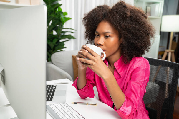 Young African businesswoman focusing project on screen monitor laptop, researching information data center on website pc and smartphone. Theme of place work in comfy room with plain color. Tastemaker. - Photo, Image