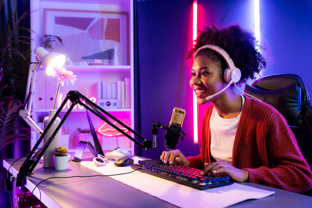 Afroamerikanische Mädchen Streamer spielen Online-Kampf mit Esport qualifizierte Team mit Kopfhörern in neonfarbener Beleuchtung Raum. Gespräche mit anderen Spielern, die Strategien planen, um Konkurrenten zu gewinnen. Geschmacksmacher. - Foto, Bild