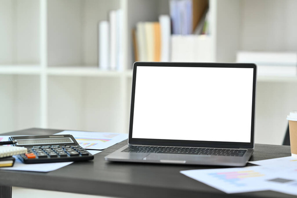 Großaufnahme-Laptop mit weißem Bildschirm, Taschenrechner und Finanzdokumenten auf schwarzem Bürotisch. - Foto, Bild