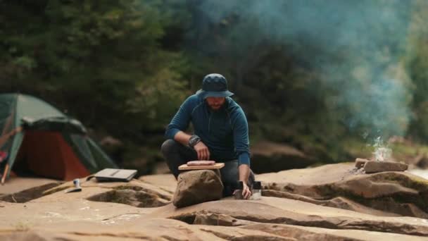 Ένας μοναχικός τουρίστας μαγειρεύει φαγητό σε μια φωτιά. Άνδρας πεζοπόρος μαγειρεύει δείπνο κοντά σε σκηνή και φωτιά, ενώ πεζοπορία στην έρημο - Πλάνα, βίντεο
