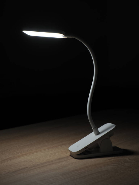 turned on rechargeable led table lamp on wooden table in dark room - Photo, Image