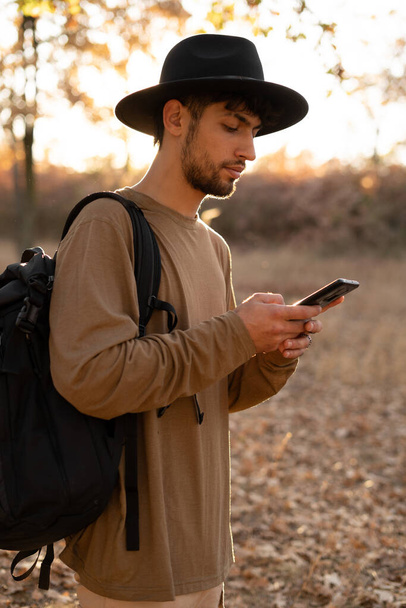 Гарний молодий мусульманин тримає телефон і використовує карти. Пішохід на природі любитель насолоджується прогулянками і свіжим повітрям в прекрасний осінній день. Копіювати простір - Фото, зображення