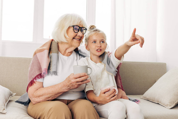 Мати жінка плетені чашки люблять дитину зима обіймає диван бабуся старша сім'я щаслива сидячи обіймаючи дочку онуку літнього способу життя дівчина диван будинок - Фото, зображення