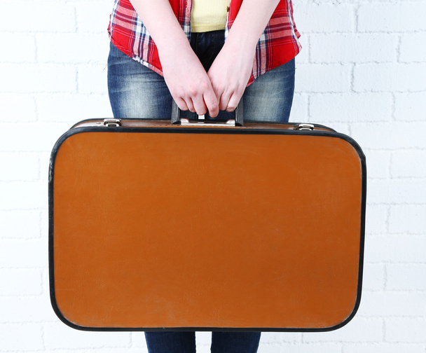 Woman holding old suitcase on brick wall background - Foto, Imagen