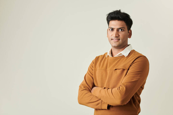 Портрет усміхненого індійського бізнесмена в гірчичному светрі, що перетинає руки і дивиться на камеру - Фото, зображення