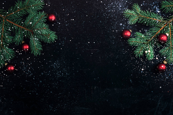 Kerstboom takken en rode ballen op zwarte achtergrond met sneeuw. Nieuwjaarsconcept. Bovenaanzicht, flat lay, kopieerruimte. - Foto, afbeelding