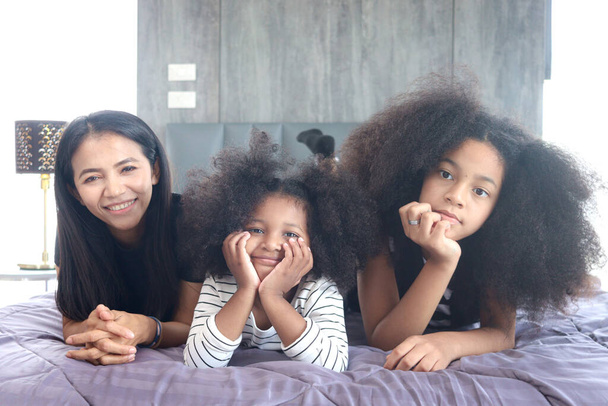 Happy family love bonding, enjoy spending time together at home, Portrait of African Asin mixed race daughter girls with curly hair and mother lying on bed in bedroom. - Foto, Bild