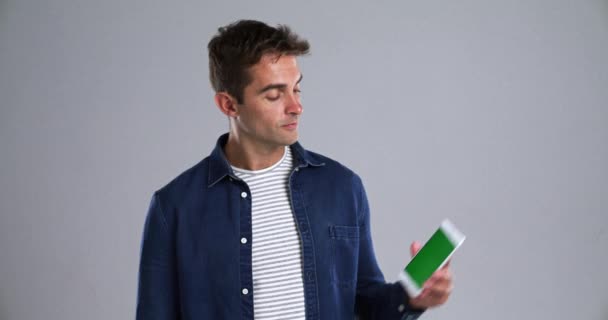 Happy man pointing at smartphone, green screen and mockup space, advertising and marketing. Portrait, phone and chroma key gesture for info, online promo or show mobile app on a grey background. - Footage, Video