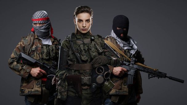 Trio de extremistas radicais do Oriente Médio em traje camo, keffiyeh e balaclava, marcando uma pose em um fundo cinza - Foto, Imagem