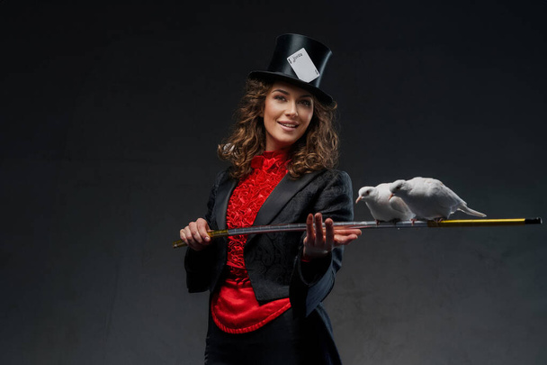 Un retrato de un mago disfrazado de magos y sombrero de copa negro realizando trucos de magia con palomas blancas contra una oscuridad - Foto, Imagen