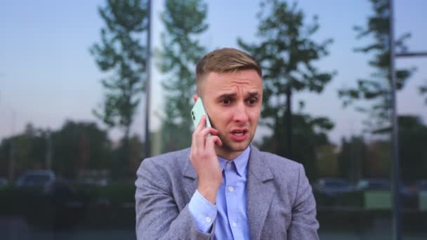 Αναστατωμένος νεαρός επιχειρηματίας μιλάει στο smartphone, κάθεται σε εξωτερικούς χώρους. Δουλειά, δουλειά, τεχνολογία. Αργή κίνηση - Πλάνα, βίντεο