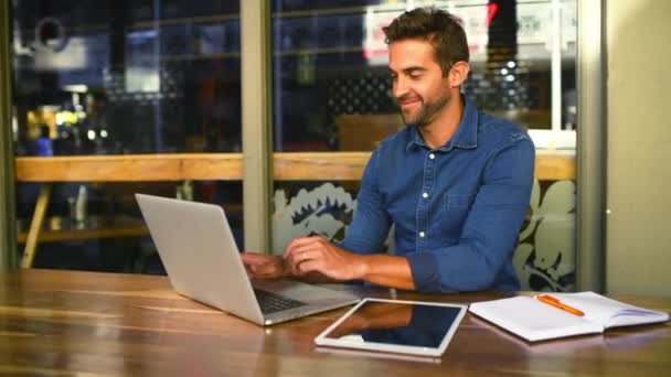 Lachen, laptop voor werk op afstand en een man in een koffieshop voor het bedrijfsleven tijdens het typen van een e-mail. Portret, technologie en papierwerk met een jonge startup ondernemer in een café als freelance medewerker. - Video