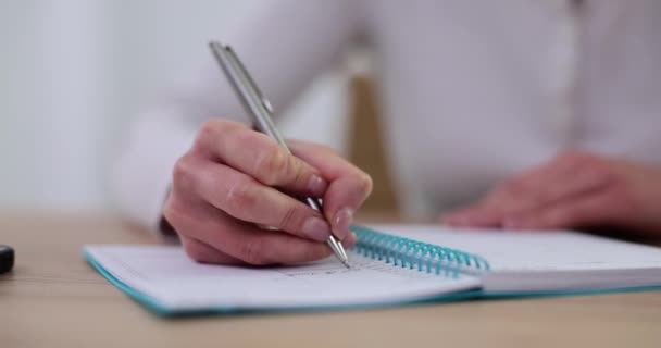 Vrouw zit aan tafel met pen, schrijft in dagboek, close-up. Zakenvrouw het opschrijven van zakelijke ideeën en startup plannen en creatieve gedachten in een notitieblok - Video