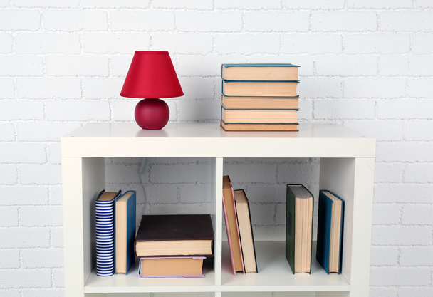 Wooden shelf with books and lamp on brick wall background - Zdjęcie, obraz