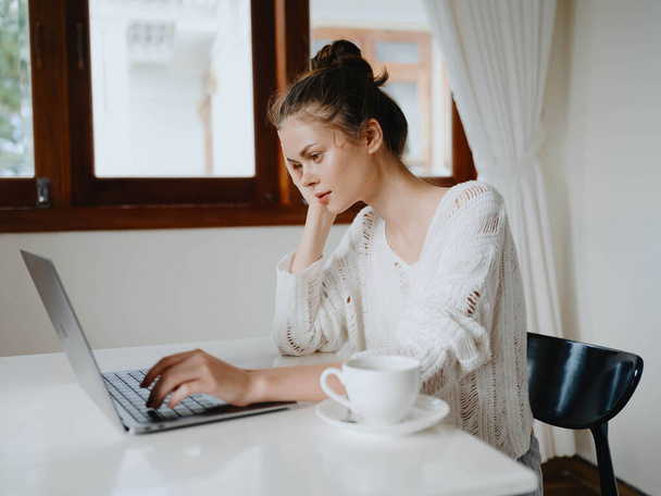 Mujer joven creativa que trabaja en un escritorio en casa en un interior acogedor con una taza de bebida, freelancer oficina en casa con una sonrisa, la comunicación y la educación en línea. Foto de alta calidad - Foto, imagen
