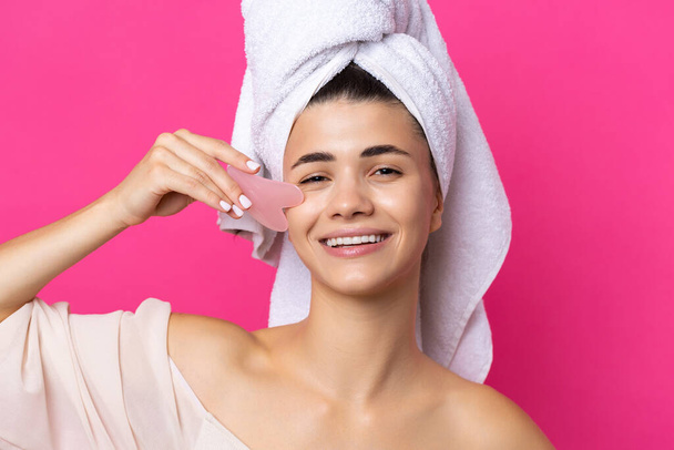 Een mooi vrolijk aantrekkelijk meisje met een handdoek op haar hoofd houdt een cosmetische hart steen dicht bij haar gezicht. - Foto, afbeelding