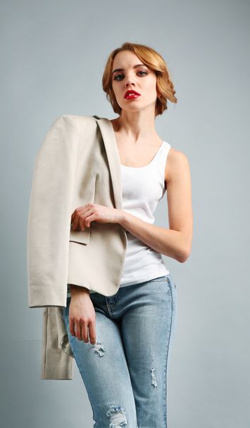 Beautiful young woman in jacket and jeans posing on light background - 写真・画像