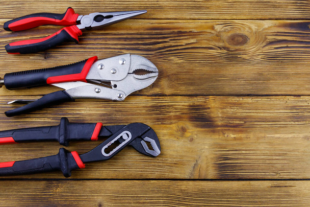 Set of different pliers on wooden background. Top view, copy space - 写真・画像