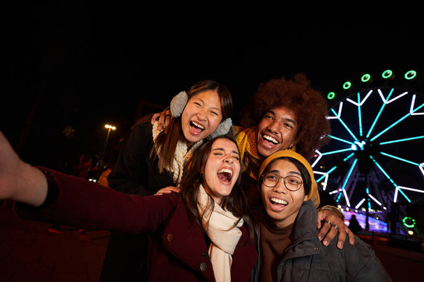 Selfie téléphone groupe multiracial de collègues heureux s'amuser en hiver. Les jeunes gens souriants z génération excités ensemble profiter de la communauté. Visage surpris d'amis au parc d'attractions la nuit.  - Photo, image
