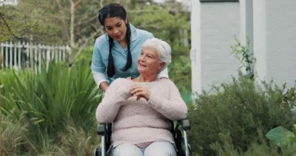Reden, Garten und eine Betreuerin mit einer Frau im Rollstuhl für Gesundheit und Morgenspaziergang. Glücklich, Pflegeheim und eine Krankenschwester im Gespräch mit einem älteren Patienten mit Behinderung auf dem Rasen zur Pflege. - Filmmaterial, Video