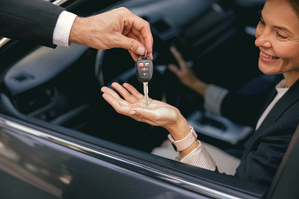 Lächelnde Geschäftsfrau erhält Schlüssel für ihr neues Statusauto vom Händler. Hochwertiges Foto - Foto, Bild
