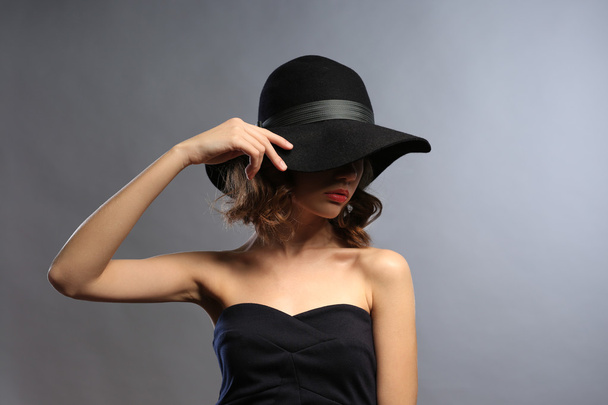 Portrait of beautiful model in black dress and hat on gray background - Photo, Image
