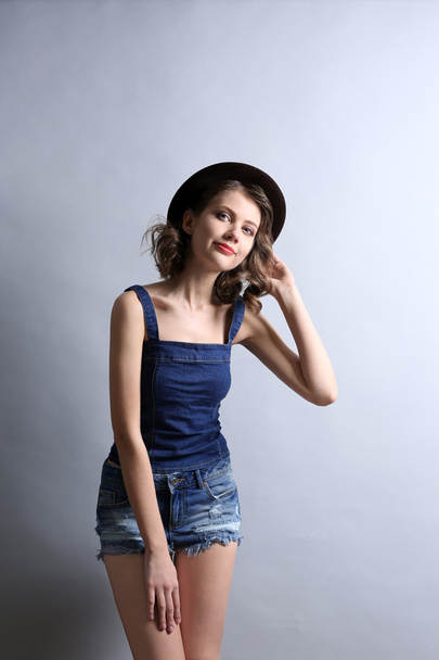 Portrait of beautiful model in jeans clothing and hat on gray background - Valokuva, kuva