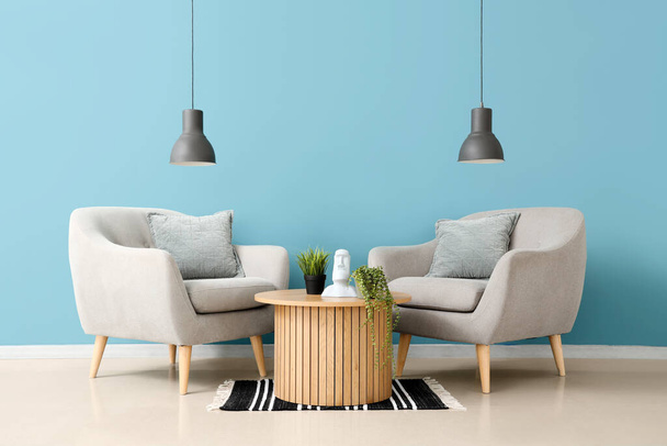 Интерьер гостиной с уютными серыми креслами и комнатными растениями на деревянном кофейном столике - Фото, изображение