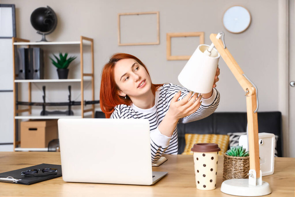 Pretty young woman changing light bulb in desk lamp at home - Photo, Image