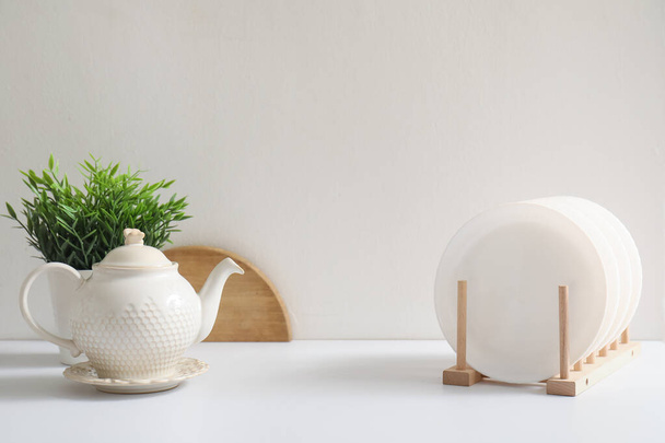 Стойка для тарелок, чайник и комод на белом кухонном столе - Фото, изображение