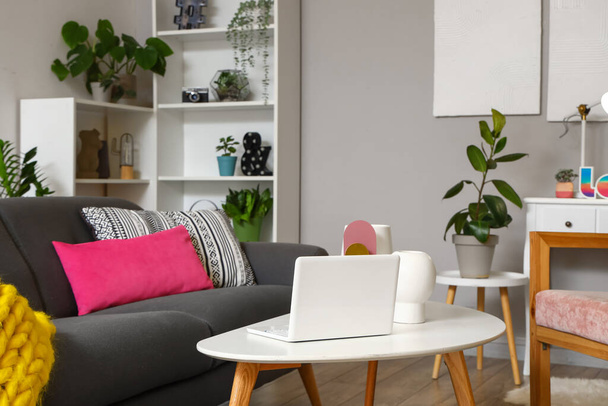Интерьер стильной гостиной с серым диваном и современным ноутбуком на кофейном столике вечером - Фото, изображение