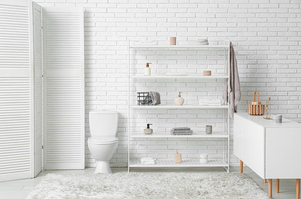 Moderna estantería con cómoda y pantalla plegable cerca de la pared de ladrillo blanco en el baño - Foto, imagen
