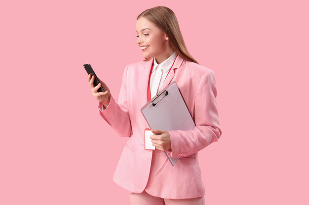 Jovem empresária com área de transferência usando telefone celular no fundo rosa - Foto, Imagem