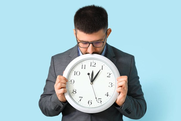 Young businessman with clock on blue background. Time management concept - Photo, Image