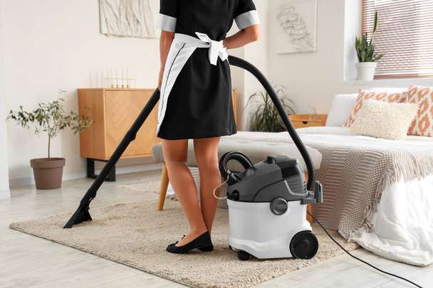 Chambermaid cleaning hotel room with vacuum cleaner - Photo, Image