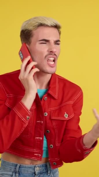 Enojado gay hombre hablando en el móvil teléfono en estudio con amarillo fondo - Metraje, vídeo