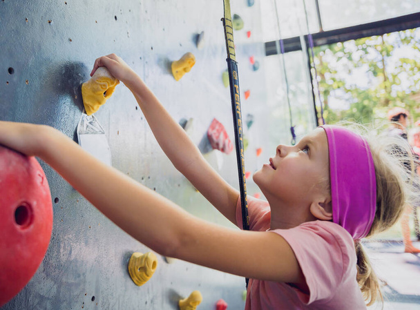 A strong baby climber climbs an artificial wall with colorful grips and ropes - Φωτογραφία, εικόνα
