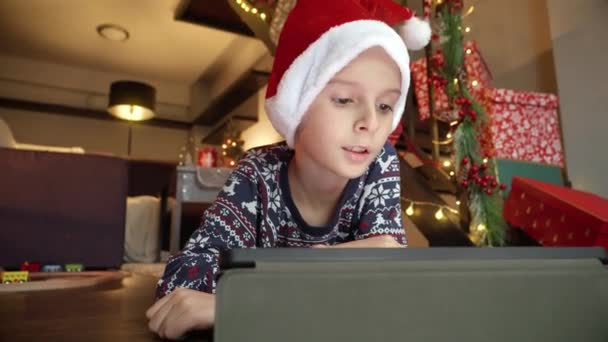Niño en la gorra de Santa tirado en el suelo y el uso de la tableta en Navidad - Imágenes, Vídeo