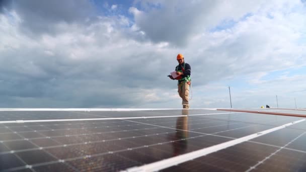 Ázsiai férfi villanyszerelő mérnök ellenőrzi telepítés napelemek fém tetőn ipari gyár séta körül holding power drill ellenőrzés fontos pontok minden napelem a vágólapon. - Felvétel, videó