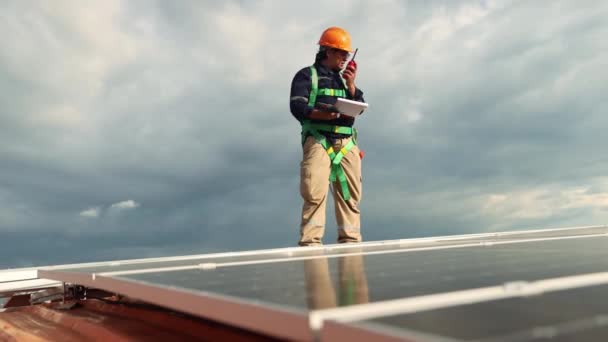 Asyalı erkek elektrik mühendisi çelik çatılı endüstriyel fabrikada güneş paneli kurulumunu inceliyor. Çatıda elinde elektrikli matkapla dolaşıyor. Her güneş panelinin önemli noktalarını kontrol et.. - Video, Çekim
