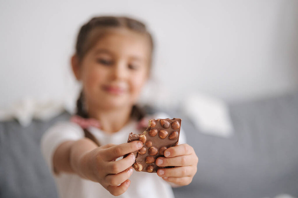 Το μικρό πανούργο κορίτσι τρώει γλυκά στο σπίτι. Το παιδί τρώει σοκολάτα και διασκεδάζει. Χάος στο σπίτι. Υψηλής ποιότητας φωτογραφία - Φωτογραφία, εικόνα