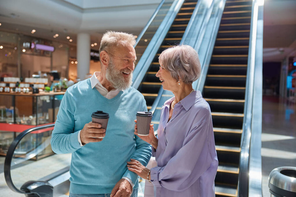 Emocionante pareja de ancianos hablando y compartiendo expresión positiva durante el tiempo de compras en el centro comercial de la ciudad - Foto, imagen